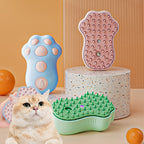 The paw-shaped misting grooming combs in blue, pink and green, with a ginger cat beside them