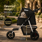 A black pet stroller with a small white dog sitting inside, shown outdoors on a stone walkway with garden plants in the background. The image includes marketing text highlighting the elevated design and seat height measurement.